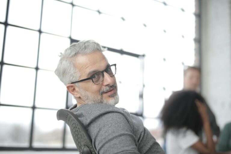 Senior confident businessman sitting in computer chair during job with colleagues in daytime